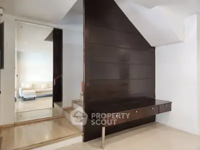 Modern interior with sleek wooden staircase and built-in storage, featuring a cozy living area in the background.