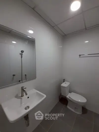 Modern bathroom with sleek fixtures and white tiles, featuring a sink, toilet, and mirror.