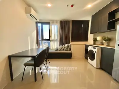 Modern apartment interior with sleek kitchen and cozy dining area, featuring a washing machine and large windows.