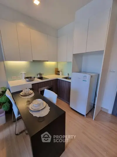 Modern kitchen with sleek cabinetry and dining area, featuring a compact fridge and elegant table setting.