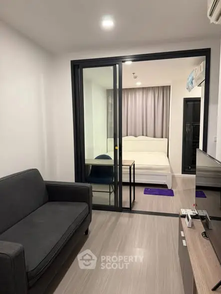 Modern apartment with sliding glass doors separating living room and bedroom, featuring sleek furniture.