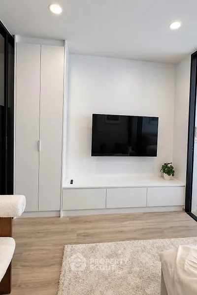 Modern living room with sleek white cabinetry and mounted TV, featuring minimalist decor and cozy ambiance.