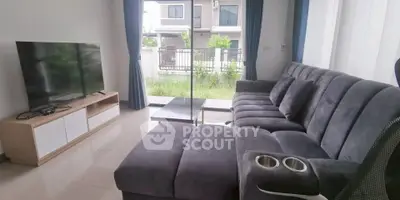 Modern living room with plush gray sectional and large TV, overlooking a garden view.