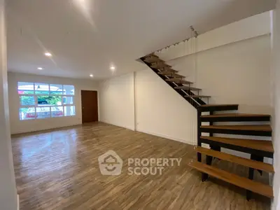 Spacious modern living room with stylish wooden staircase and large window view.
