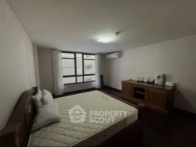 Spacious bedroom with large window and wooden furniture, perfect for comfort and relaxation.