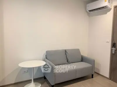 Cozy minimalist living room with gray sofa and white side table, featuring modern air conditioning.