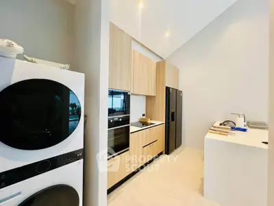 Modern kitchen with sleek appliances and wood cabinetry, featuring a stacked washer and dryer.