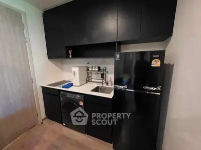 Modern kitchen with sleek black cabinets, washing machine, and compact fridge in a stylish apartment.