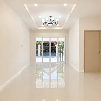 Spacious modern living room with elegant chandelier and large glass doors leading to a serene outdoor view.