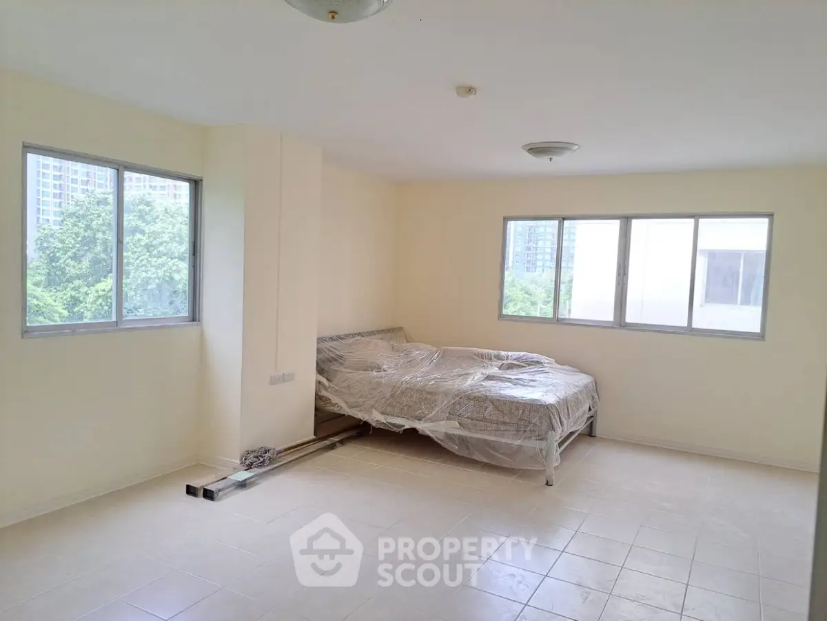 Spacious bedroom with large windows and natural light in modern apartment.