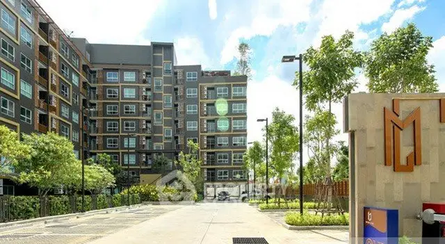 Modern apartment building with lush greenery and spacious parking area.