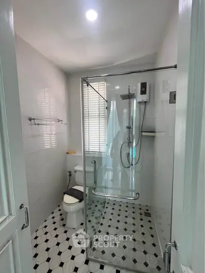 Modern bathroom with glass shower enclosure and stylish black-and-white tile flooring.