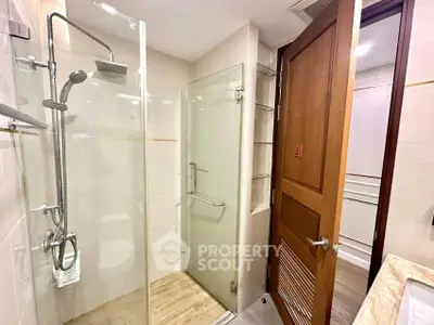 Modern bathroom with glass shower enclosure and wooden door, featuring sleek fixtures and bright lighting.
