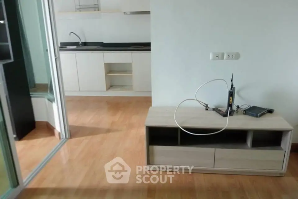 Modern apartment interior with open kitchen and wooden flooring, featuring a sleek TV stand.