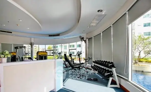 Spacious gym with modern equipment and large windows offering natural light.