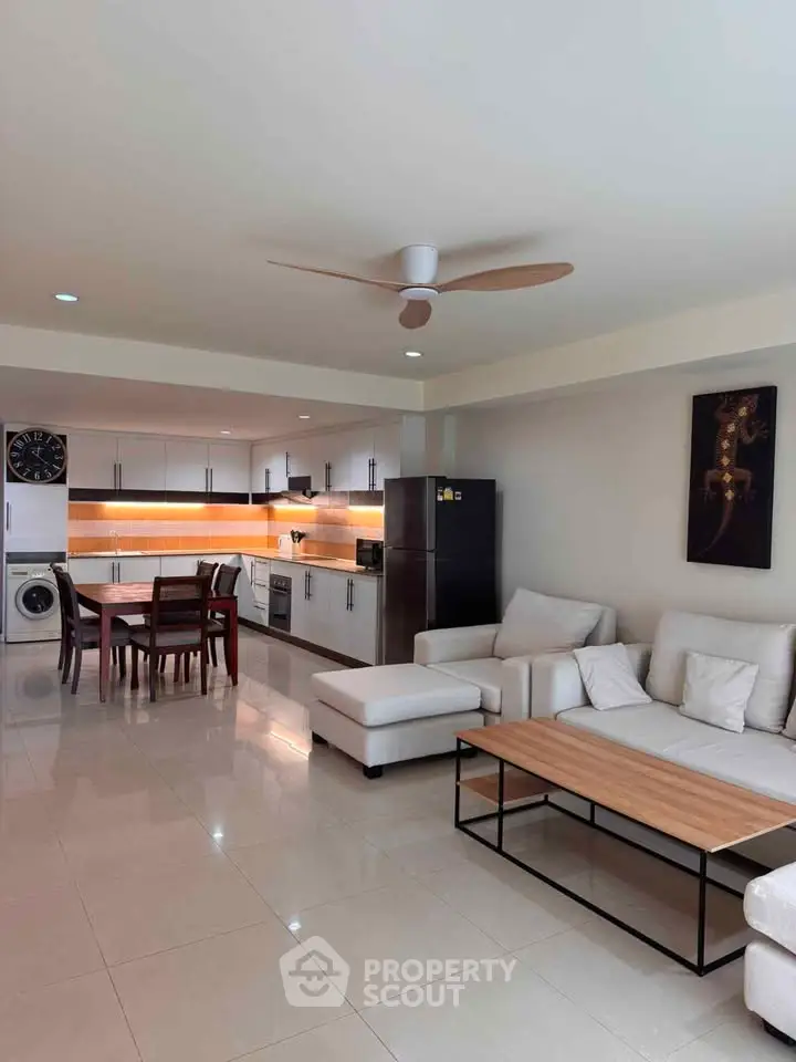 Spacious modern living room with open kitchen, featuring sleek furniture and appliances, ideal for contemporary living.