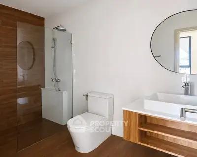 Modern bathroom with glass shower, wooden accents, and round mirror.