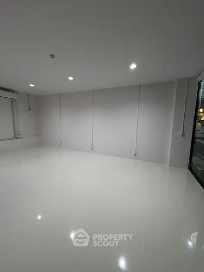 Spacious unfurnished room with glossy white tiles and modern lighting, ideal for customization.