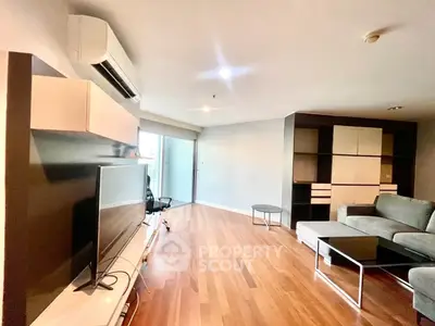 Spacious modern living room with sleek furniture and large TV, featuring wooden flooring and ample natural light.