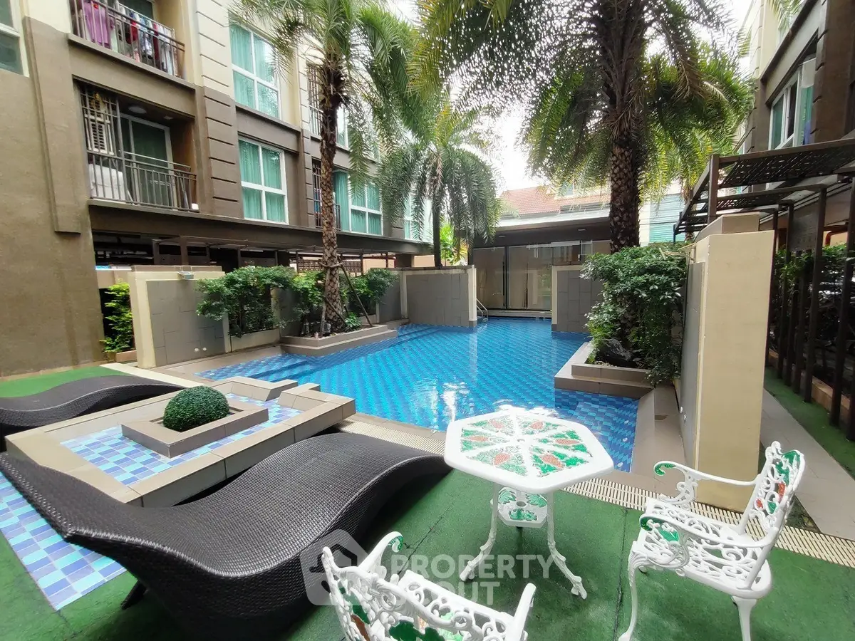 Luxurious poolside area with elegant seating and lush greenery in a modern apartment complex.