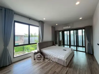 Spacious modern bedroom with large windows and balcony access, featuring elegant hardwood floors and stylish decor.