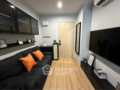 Modern living room with sleek black sofa, wooden flooring, and wall-mounted TV in stylish apartment.