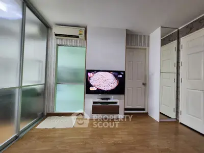 Modern living room with TV and wooden flooring, featuring sliding glass doors and air conditioning.