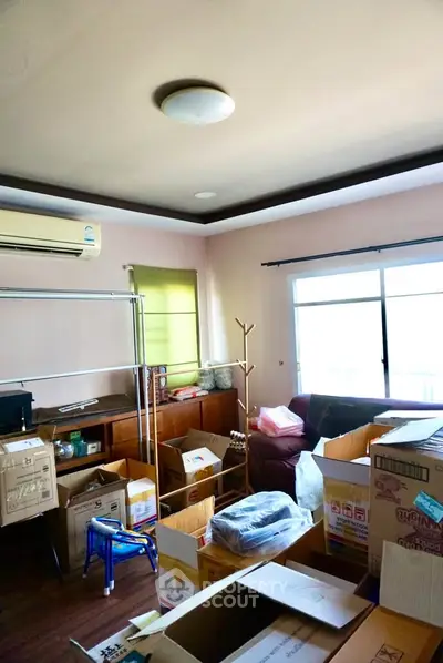 Spacious living room with moving boxes, air conditioning, and large windows for natural light.