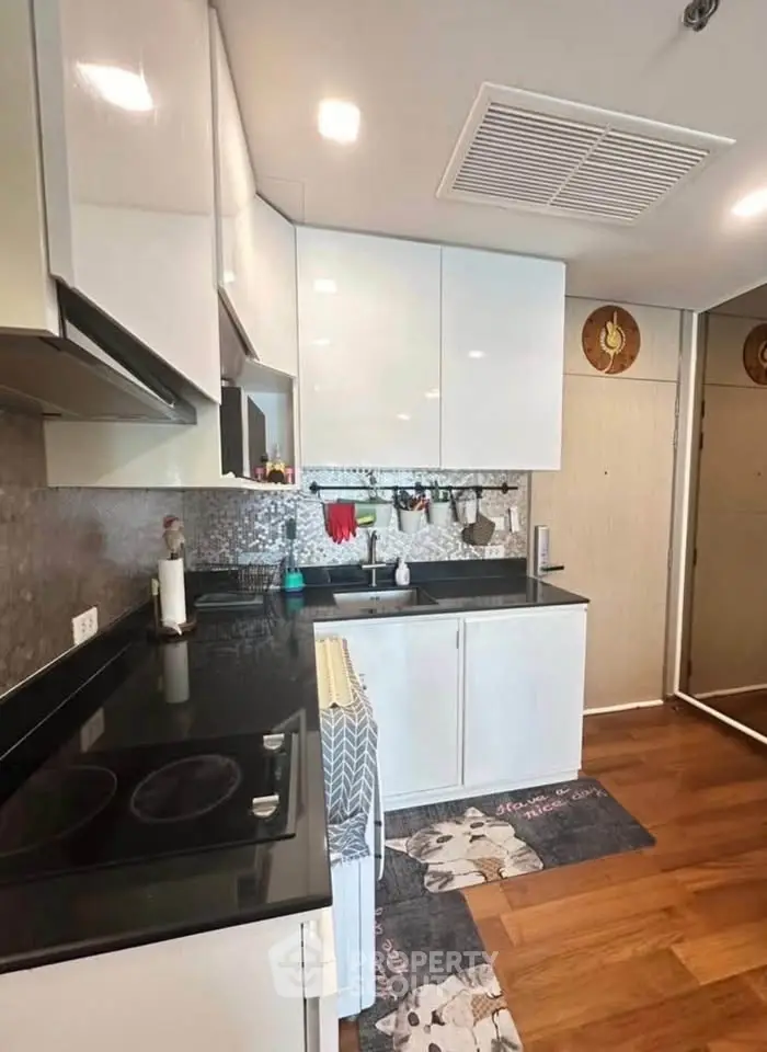 Modern kitchen with sleek white cabinets and black countertops, featuring a stylish backsplash and wooden flooring.