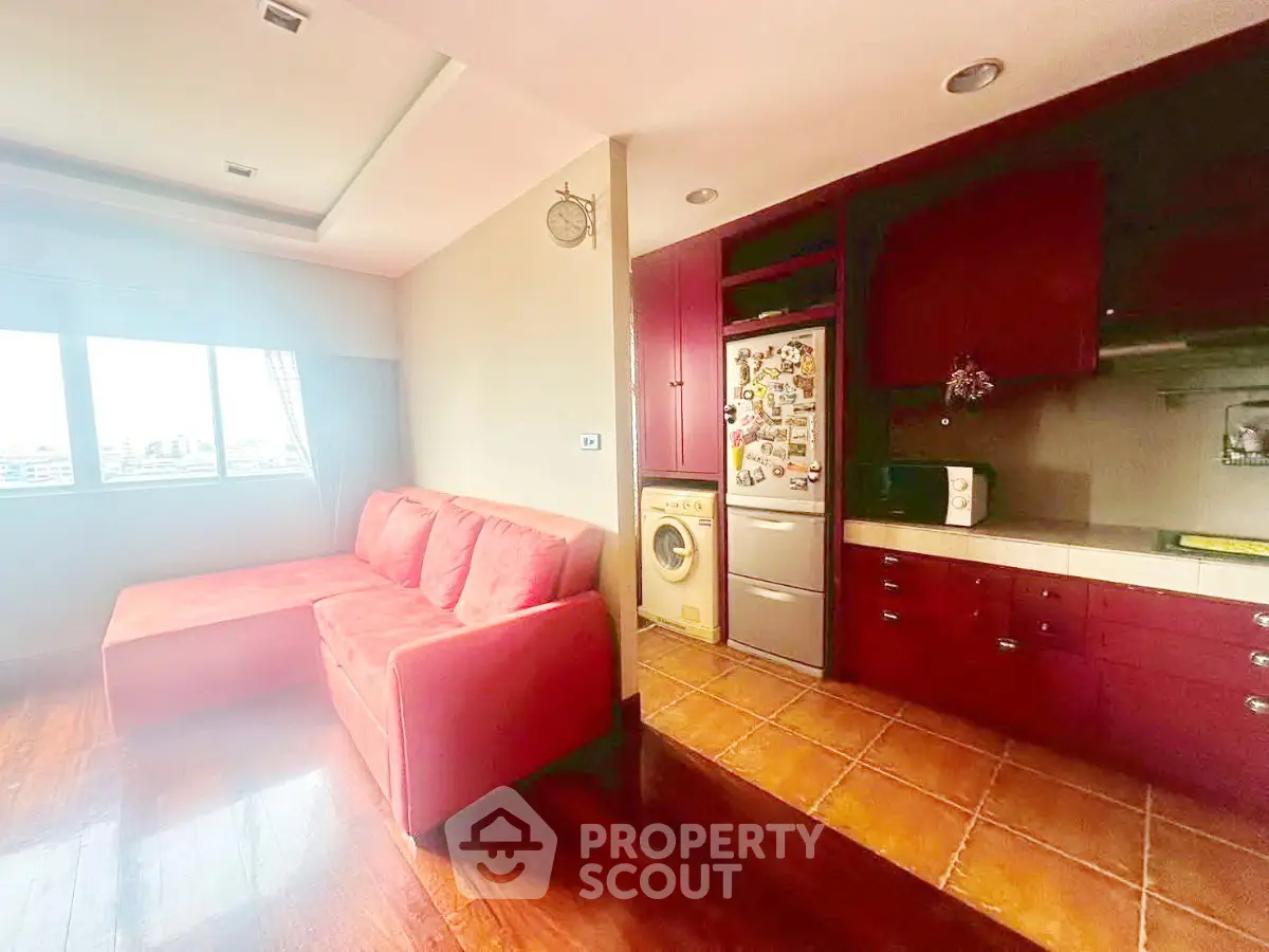 Spacious living room with modern kitchen and vibrant red sofa, featuring a washing machine and fridge.