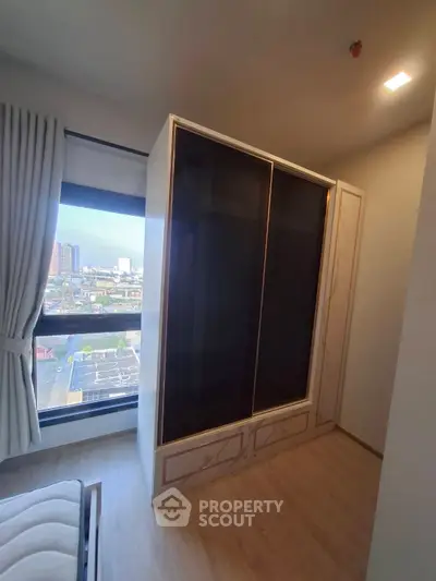 Modern bedroom with large window and sleek wardrobe offering city views.