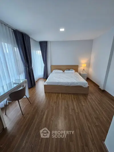 Spacious modern bedroom with wooden flooring and large windows for natural light.