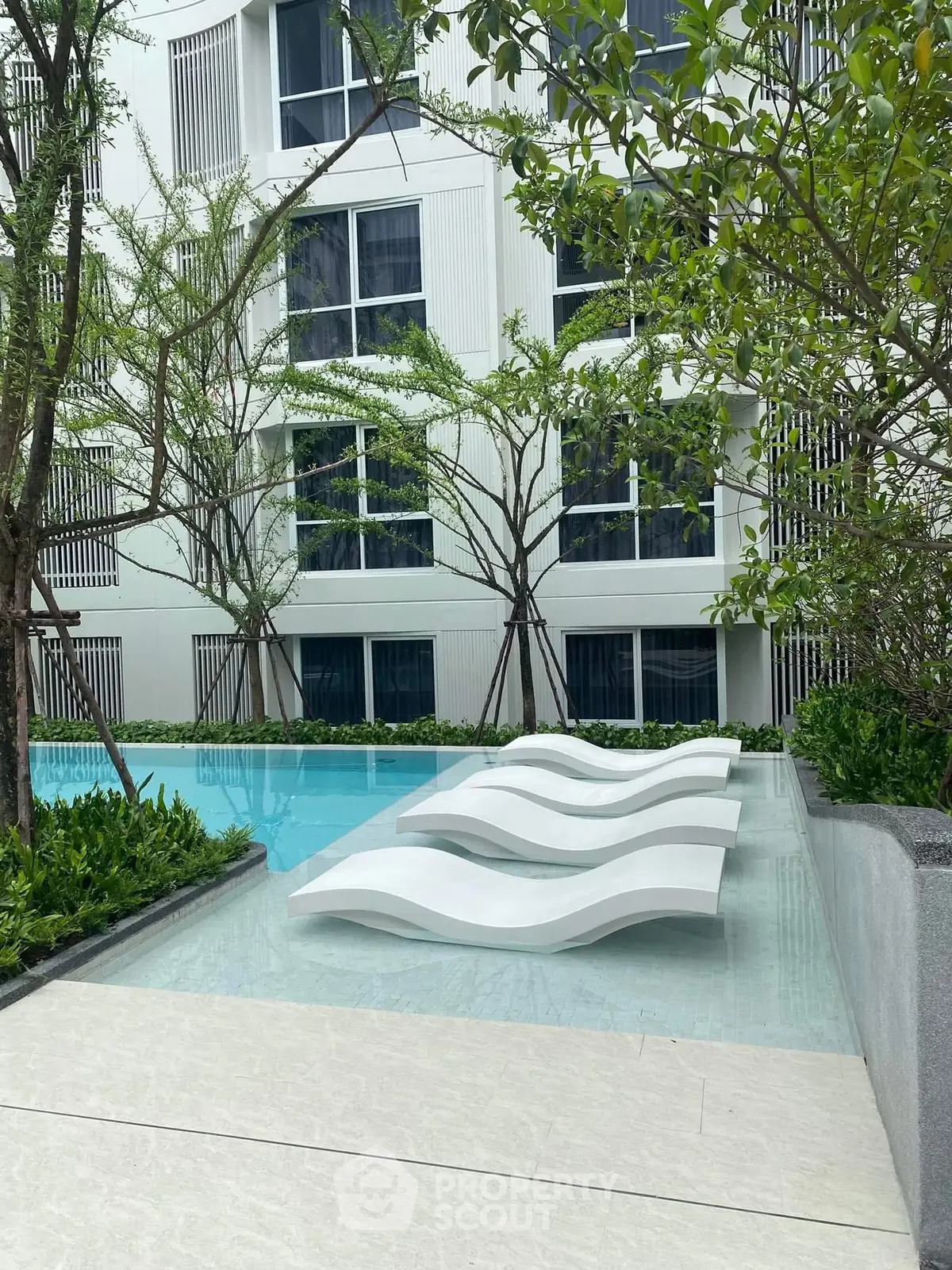 Modern apartment pool area with stylish lounge chairs and lush greenery