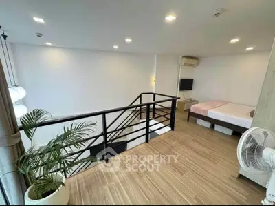 Modern loft bedroom with sleek railing and wooden flooring, featuring a cozy bed and stylish decor.