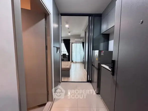 Modern apartment hallway leading to a cozy bedroom with sleek kitchen appliances.