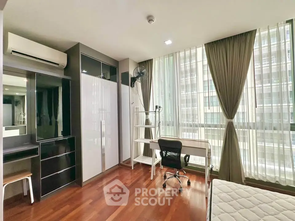 Spacious bedroom with modern furniture and large windows in a high-rise apartment.