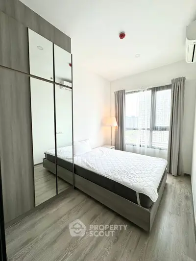 Modern minimalist bedroom with large window and mirrored wardrobe in high-rise apartment.