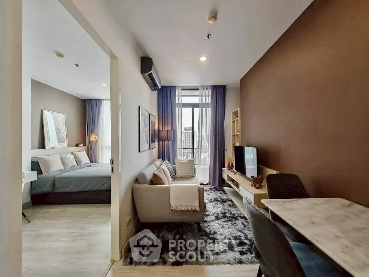 Modern open-plan living room with cozy seating and stylish decor, leading to a bright bedroom with large windows.