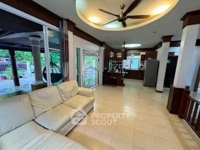 Spacious living room with open kitchen and garden view, featuring modern ceiling fan and cozy seating.