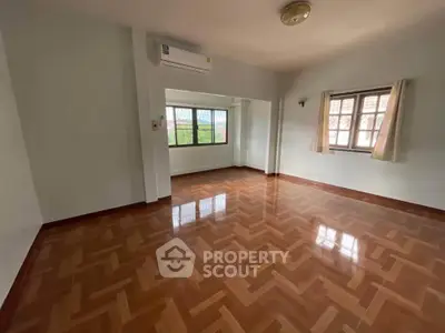 Spacious empty room with wooden flooring and large windows, perfect for customization.