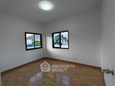 Bright empty room with wooden flooring and large windows in modern home.