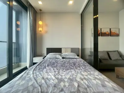Modern bedroom with geometric bedding and glass partition, featuring a cozy seating area and stylish decor.