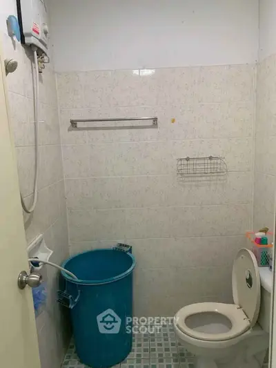 Compact bathroom with essential fixtures and tiled walls, featuring a blue bucket and a wall-mounted water heater.