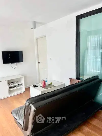 Modern living room with sleek black sofa, wall-mounted TV, and wooden flooring.