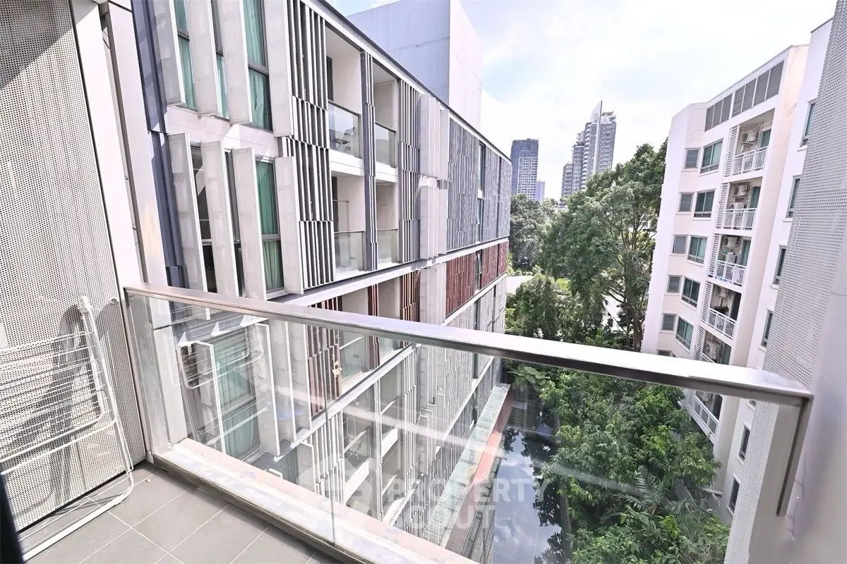 Modern urban apartment view with glass balcony overlooking cityscape and greenery.