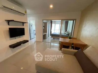 Modern open-plan living room with cozy sofa, wall-mounted TV, and view into a stylish bedroom.