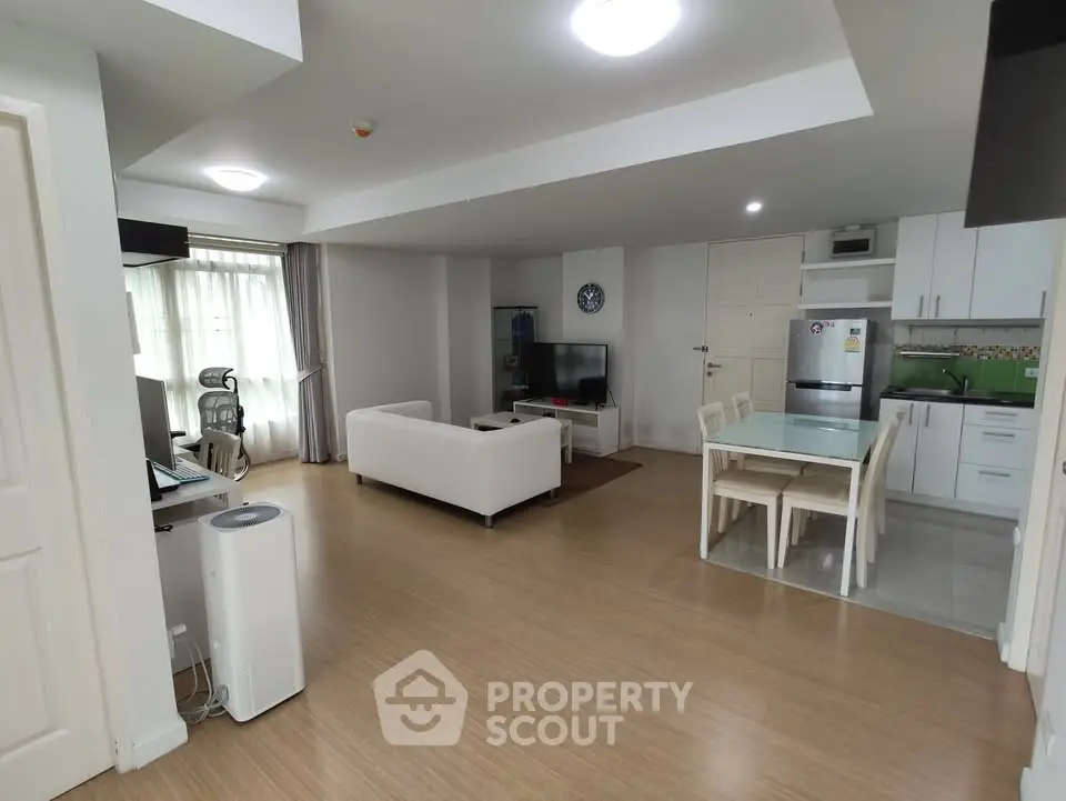 Spacious open-plan living room with modern kitchen and dining area, featuring sleek furniture and natural light.