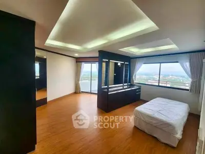 Spacious bedroom with large windows offering stunning city views and modern wooden flooring.