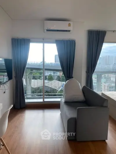 Modern living room with large window and city view, featuring sleek furniture and wooden flooring.