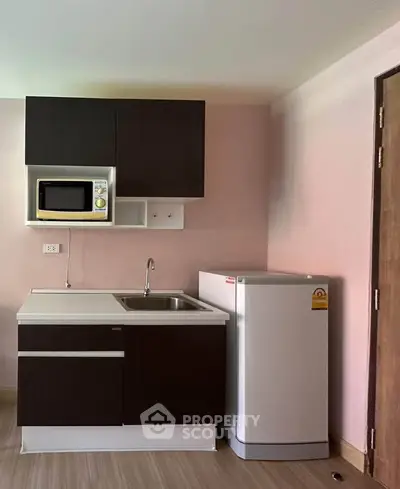 Compact kitchen with dark cabinets, microwave, and fridge in modern apartment.